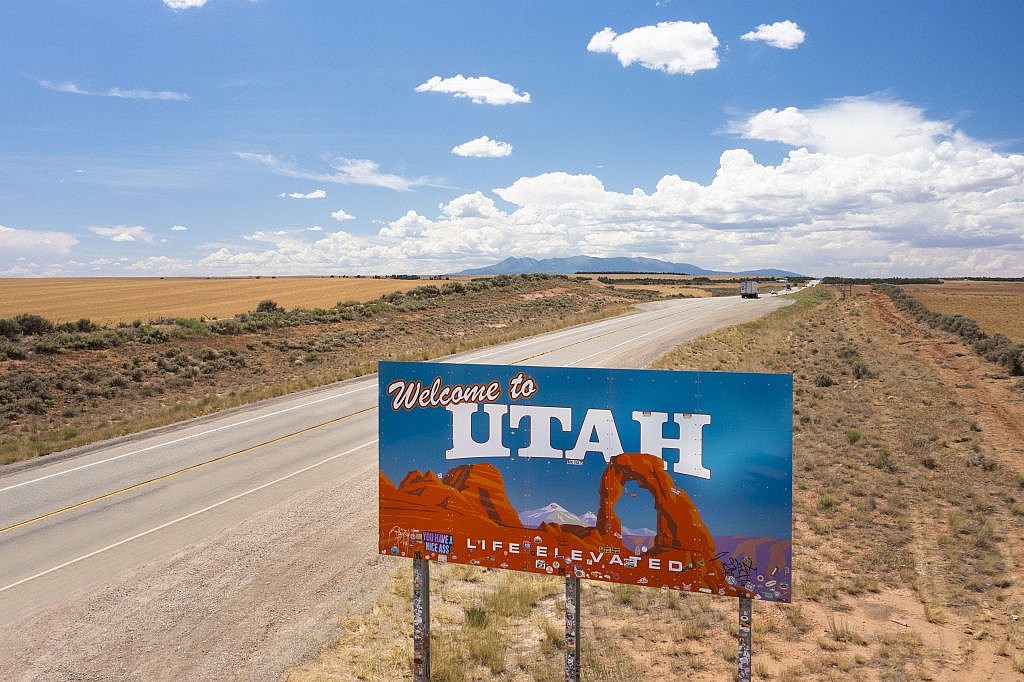 Welcome to Utah sign with a long road and mountains in the background
