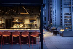 Evening detail of Aire rooftop bar with red stools and interior bar lighting.