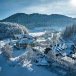Winter aerial view of Arabella Jagdhof Resort surrounded by snowy alpine forest and mountains
