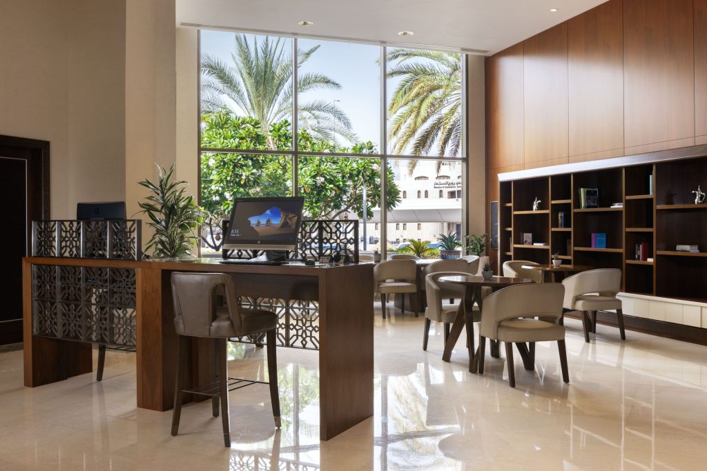 Lobby lounge at Sheraton Muscat with café seating and palm-lined window view.