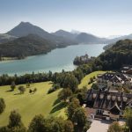 Summer drone view of Lake Fuschlsee with rolling hills and resort visible below