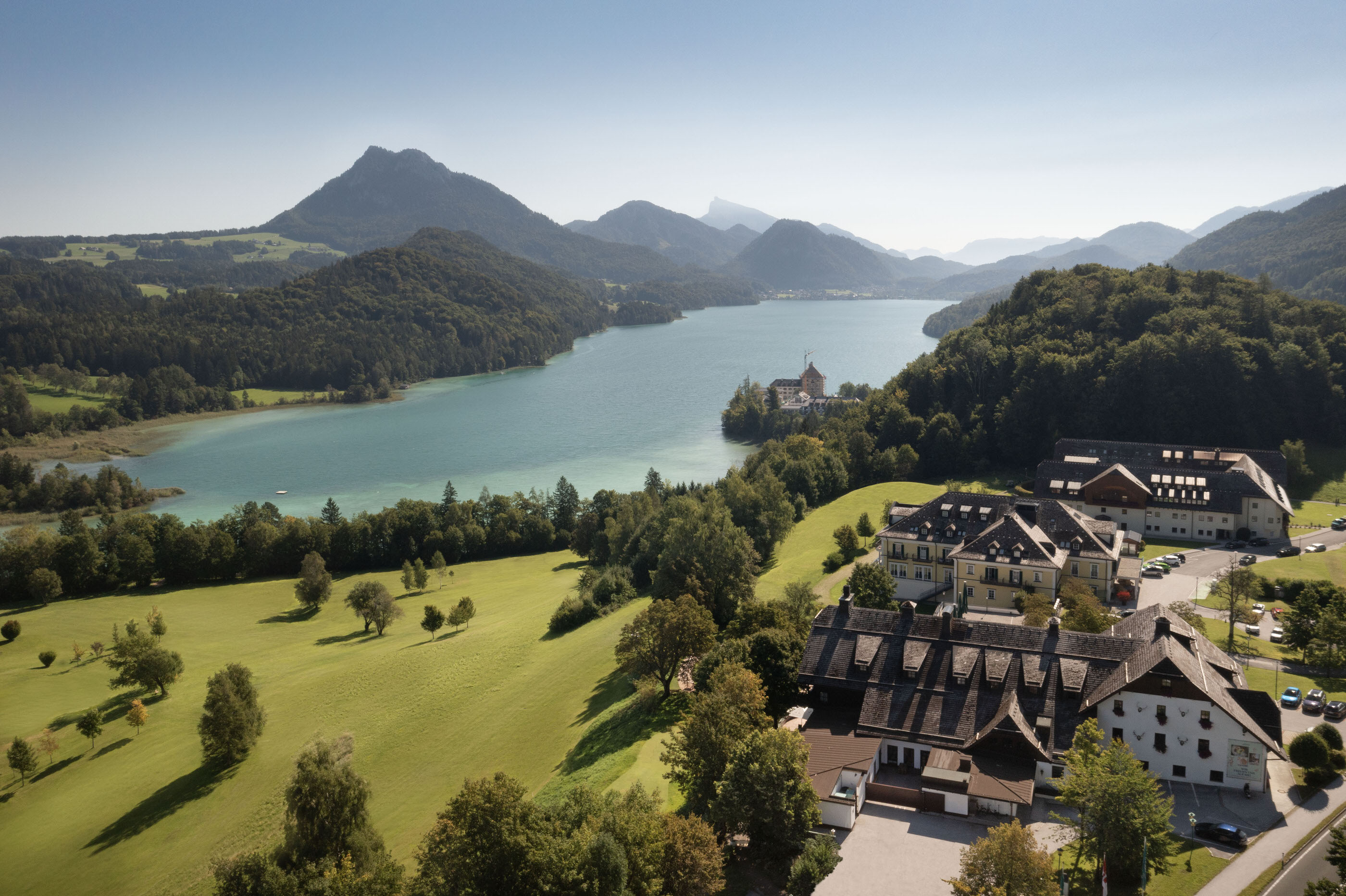 Summer drone view of Lake Fuschlsee with rolling hills and resort visible below