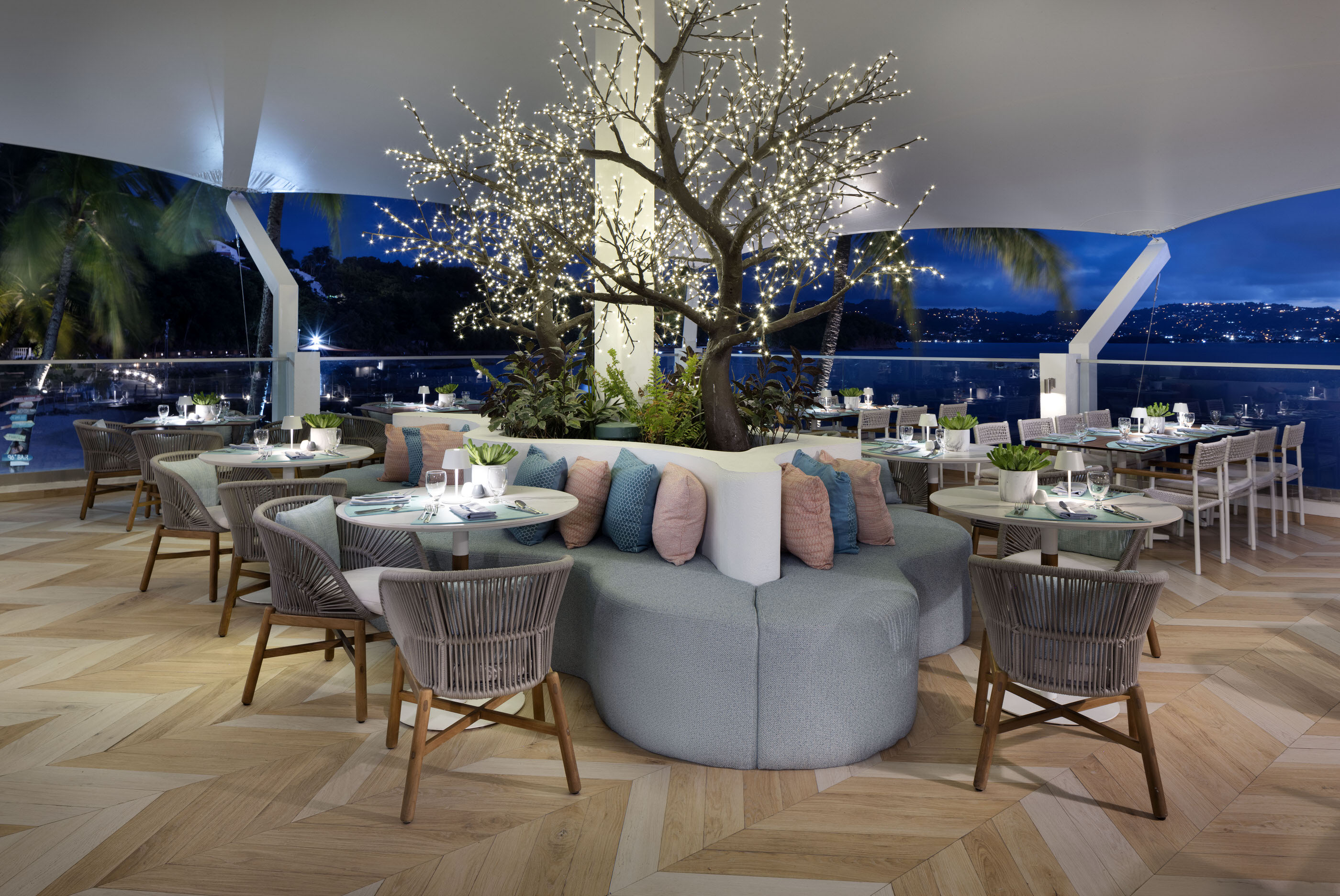 Evening dining setup at Windjammer Landing with central tree feature and a view of Castries lights in the distance.