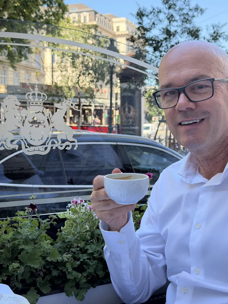 Steven Graffham holding a cup of coffee at a terrace table at Café Imperial Wien