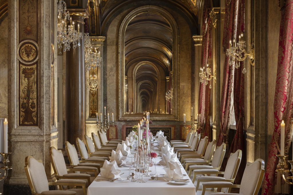 Formal dining table extending through a richly decorated chandelier-lit hall at Hotel Imperial Vienna